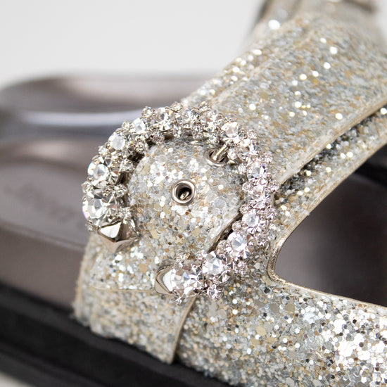 Sandals with silver glittery straps and buckle details on a white background