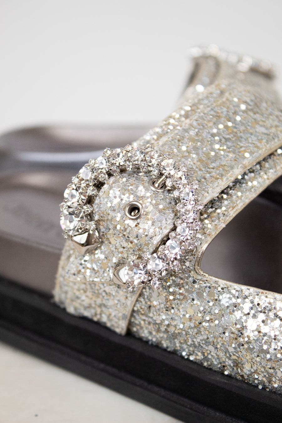 Sandals with silver glittery straps and buckle details on a white background