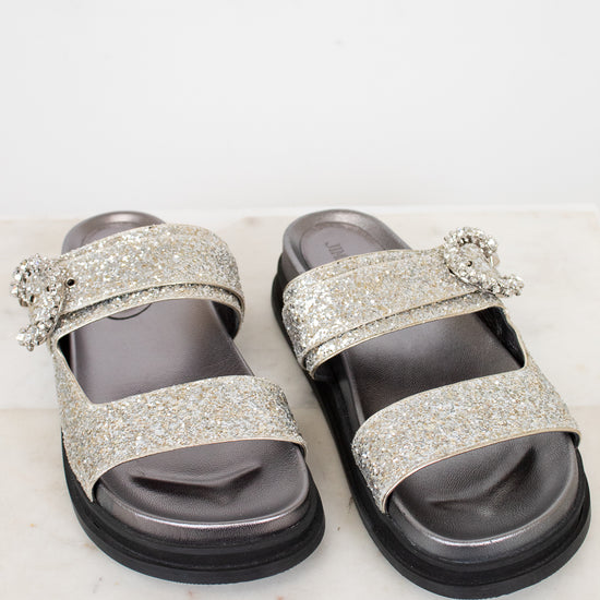 Silver glitter sandals with embellishments on a white marble surface
