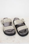 Silver glitter sandals with embellishments on a white marble surface