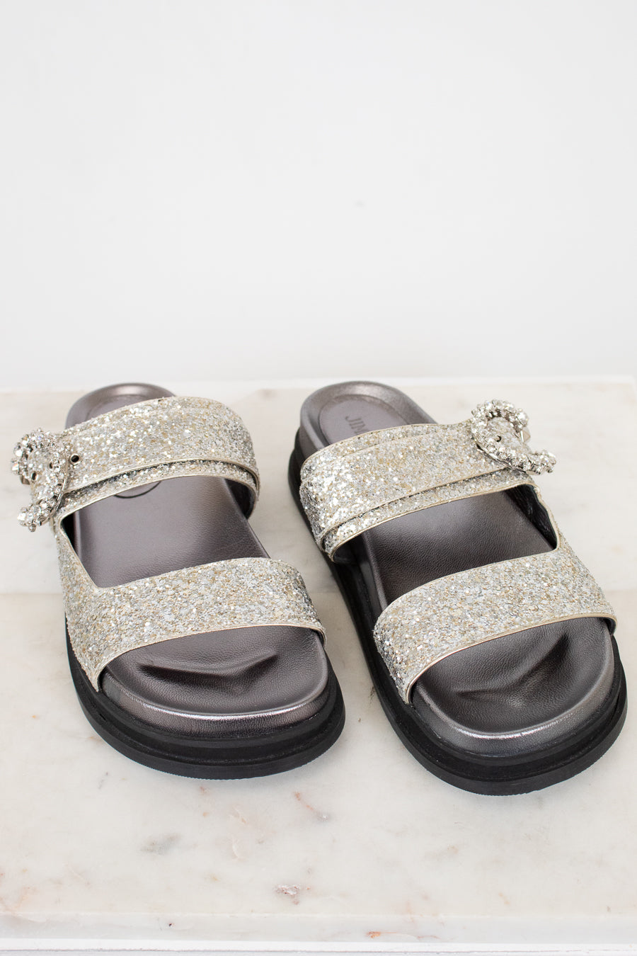 Silver glitter sandals with embellishments on a white marble surface