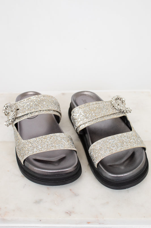 Silver glitter sandals with embellishments on a white marble surface