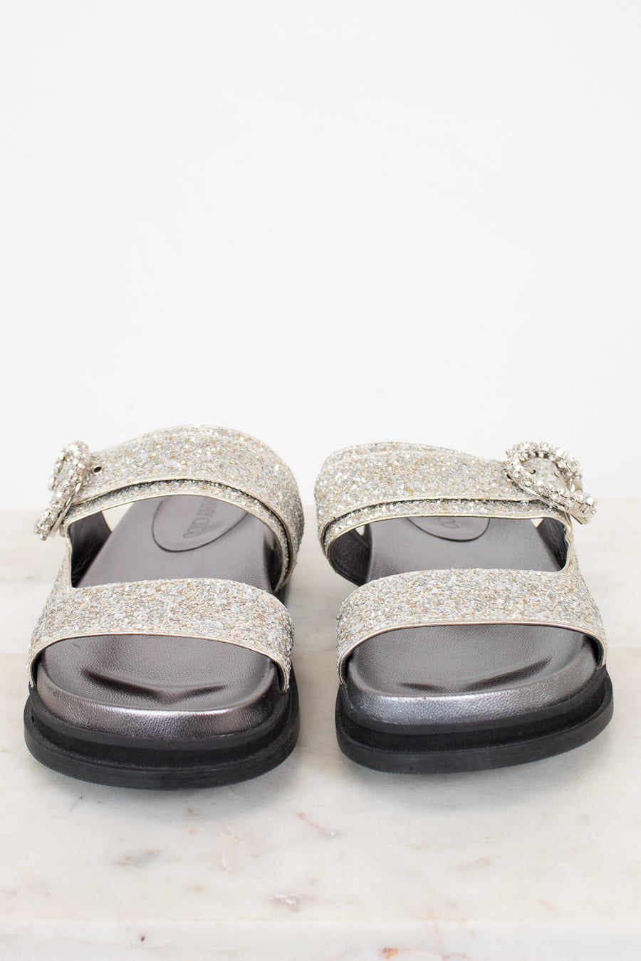 Silver glittery sandals with decorative straps on a white background