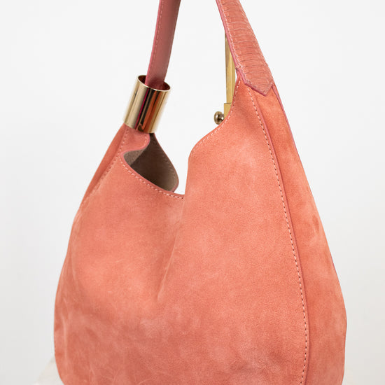Pink suede handbag with gold accents on a white background