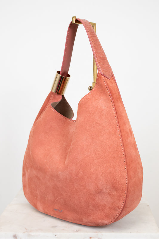 Pink suede handbag with gold accents on a white background