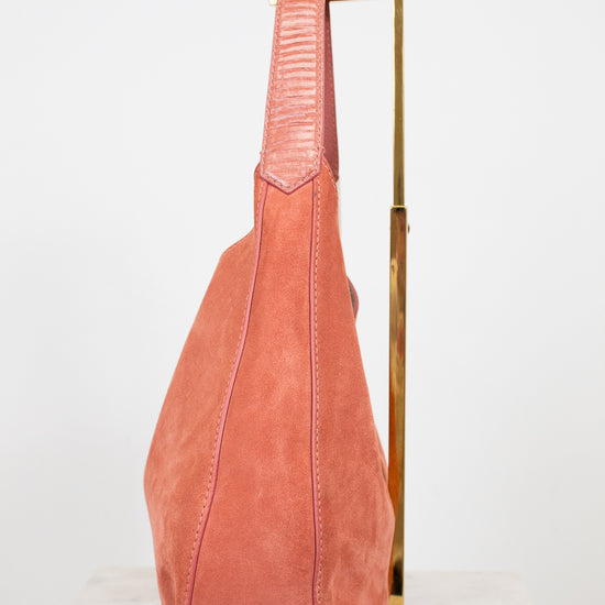 Pink suede bag on a gold stand against a white background