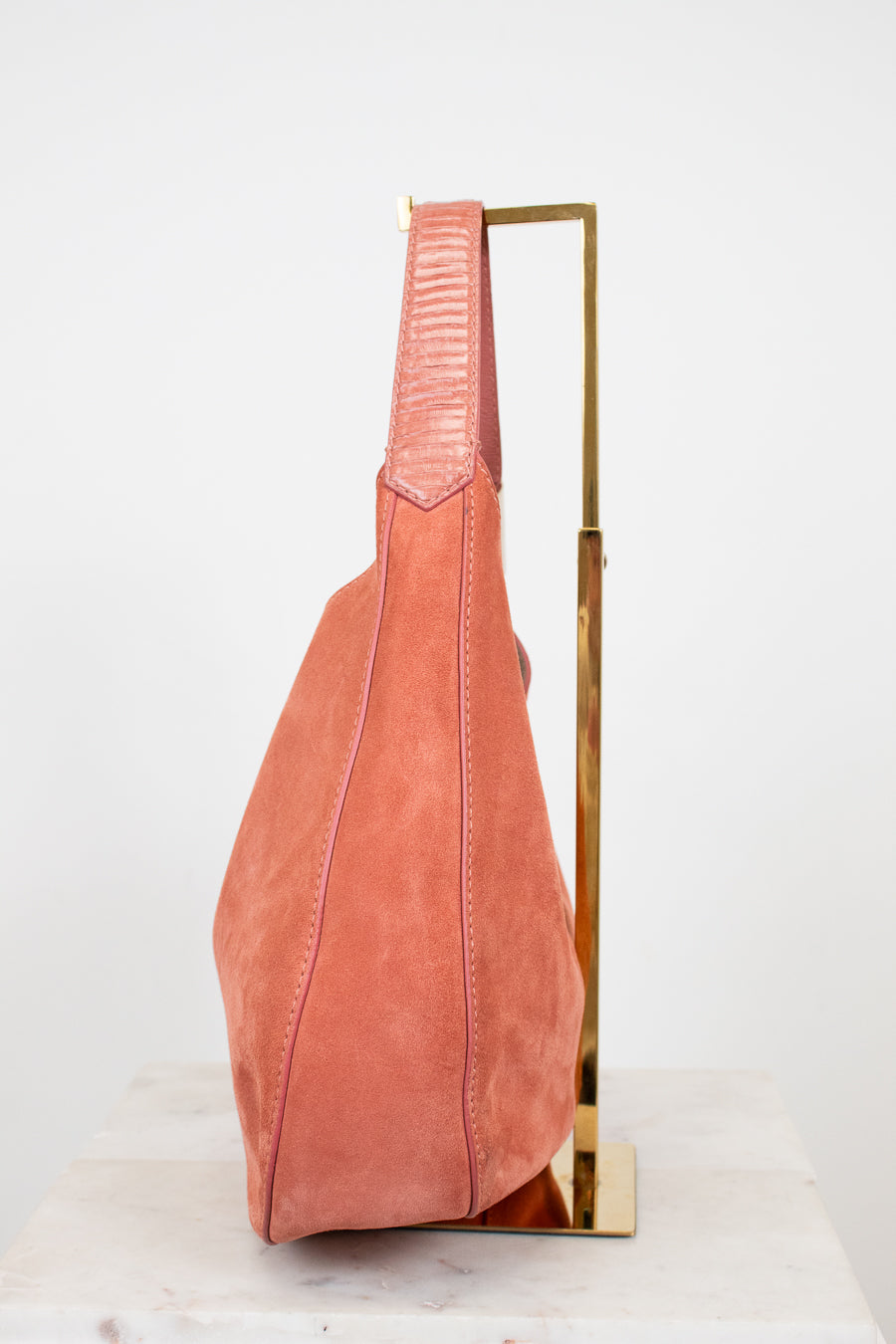 Pink suede bag on a gold stand against a white background