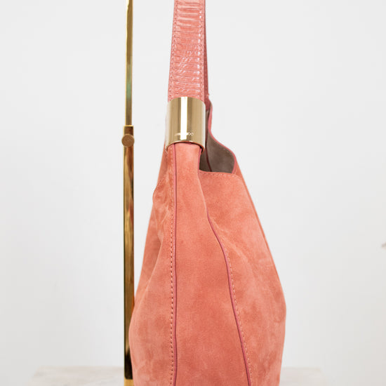 Pink suede handbag with gold accents on a white background
