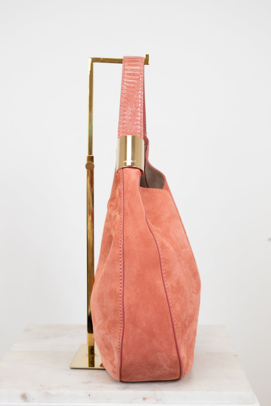 Pink suede handbag with gold accents on a white background