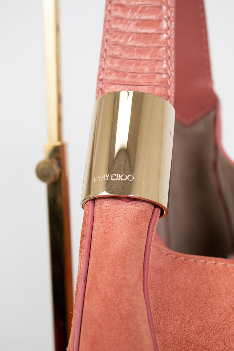 Close-up of a pink handbag with a gold clasp featuring 'Jimmy Choo' branding.