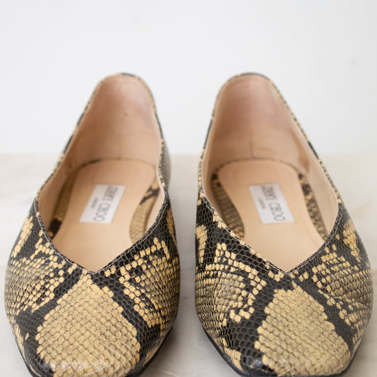 A pair of Jimmy Choo snakeskin ballet flats with a beige, black, and brown python pattern, shown on a light marble surface against a white background.