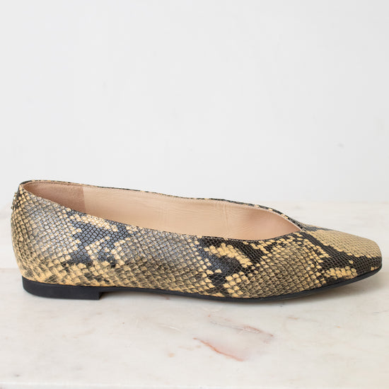 A single women's flat shoe with a snakeskin pattern in beige, brown, and black, shown from the side on a light marble surface against a white background.