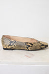 A single women's flat shoe with a snakeskin pattern in beige, brown, and black, shown from the side on a light marble surface against a white background.