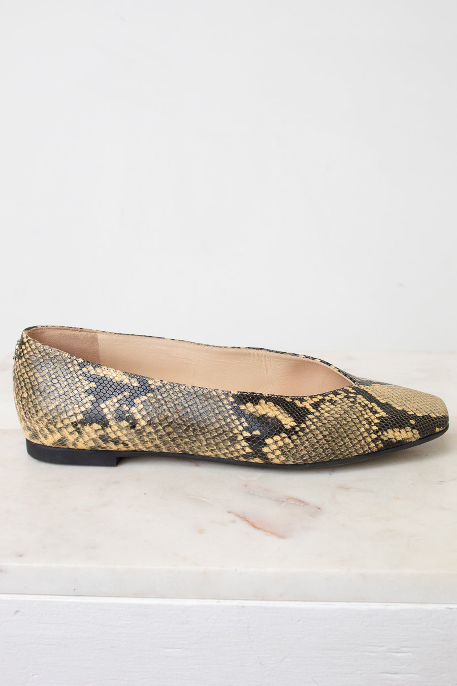 A single women's flat shoe with a snakeskin pattern in beige, brown, and black, shown from the side on a light marble surface against a white background.