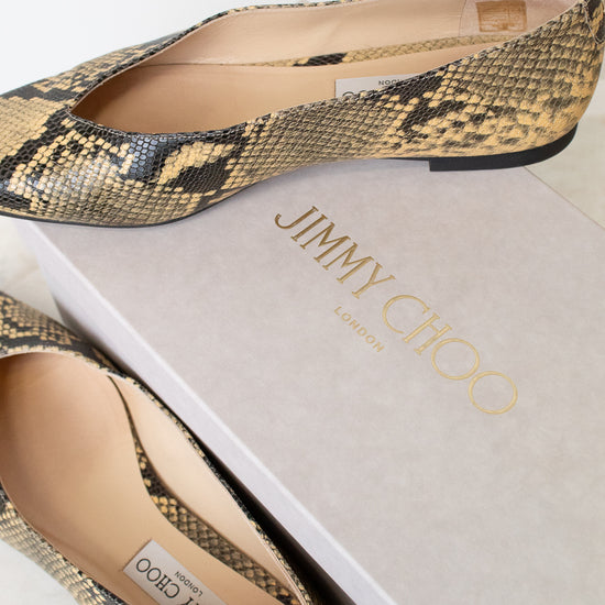 A pair of Jimmy Choo London pointed-toe flat shoes in a snakeskin pattern, displayed on top of and next to their light gray brand box.