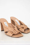Pair of tan high-heeled sandals with a knot detail on a white background