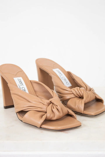 Pair of tan high-heeled sandals with a knot detail on a white background