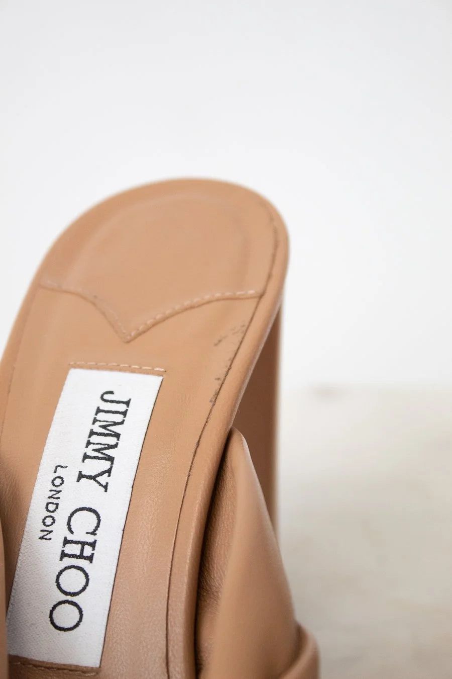 Close-up of a tan sandal with a Jimmy Choo label on a white background