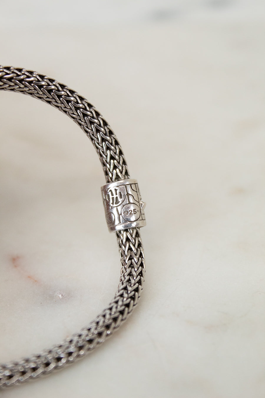 Silver braided bracelet with a clasp on a marble surface