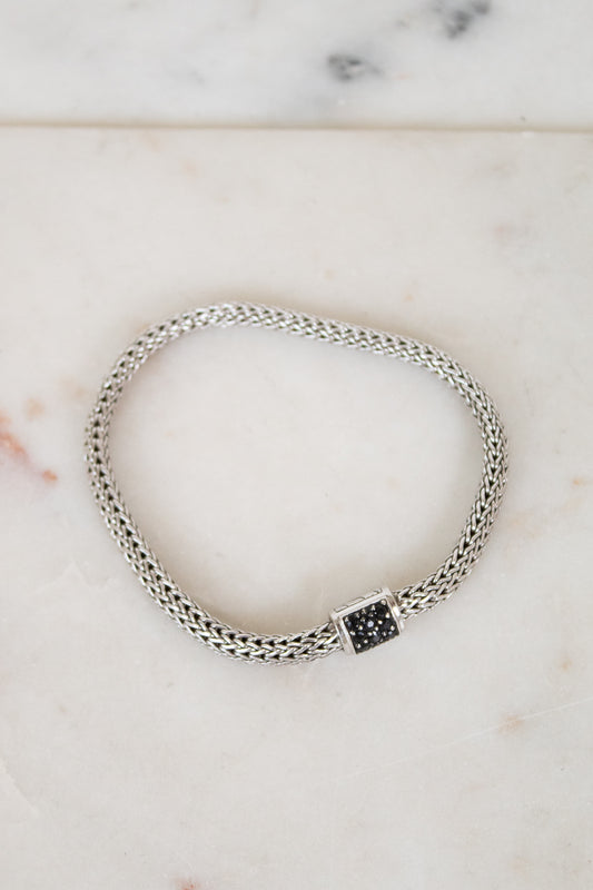 Silver braided bracelet with small black sapphires on a white marble background
