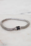 Silver bracelet with black gemstone clasp on a marble surface
