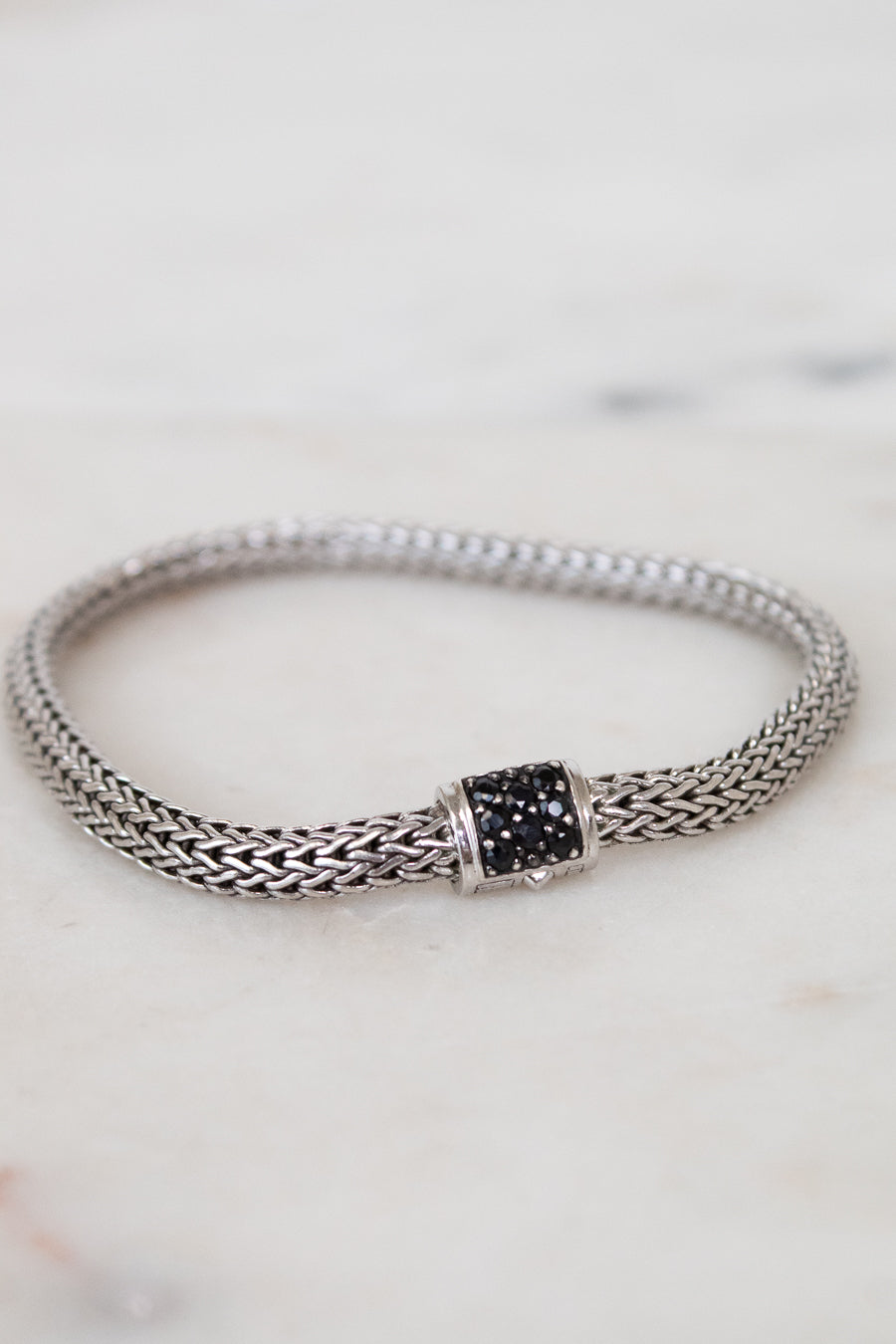 Silver bracelet with black gemstone clasp on a marble surface