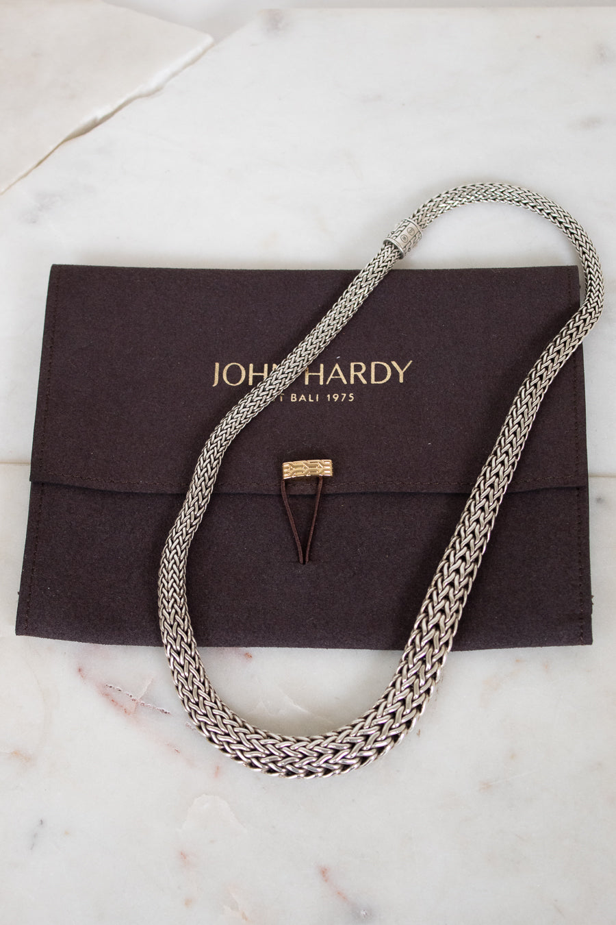 Silver chain necklace on a John Hardy pouch with a marble background