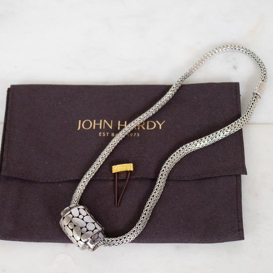 Silver necklace on a John Hardy branded pouch with a white background