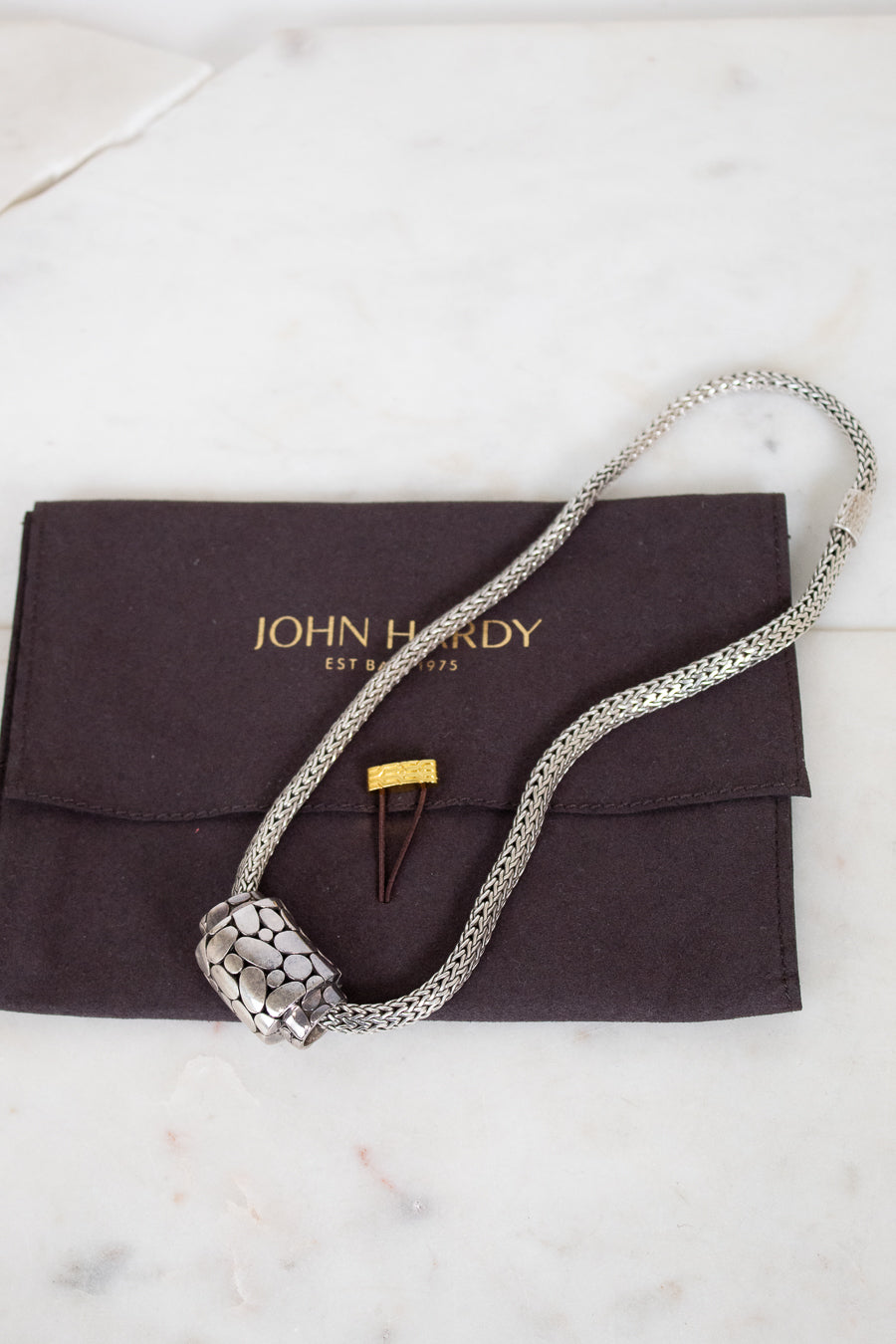 Silver necklace on a John Hardy branded pouch with a white background