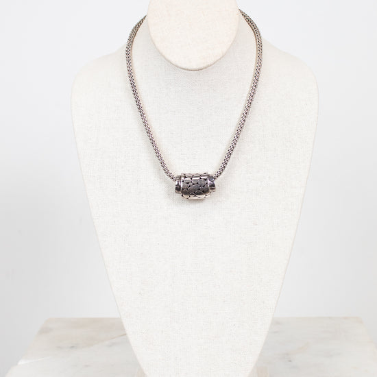 Silver necklace on a white stand with a marble base