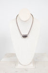 Silver necklace on a white stand with a marble base
