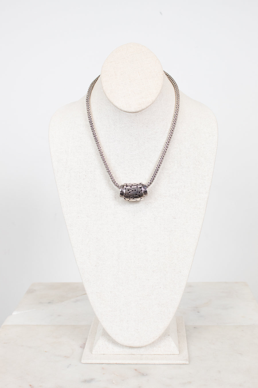 Silver necklace on a white stand with a marble base