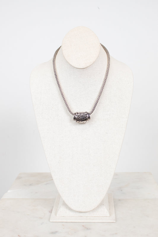 Silver necklace on a white stand with a marble base