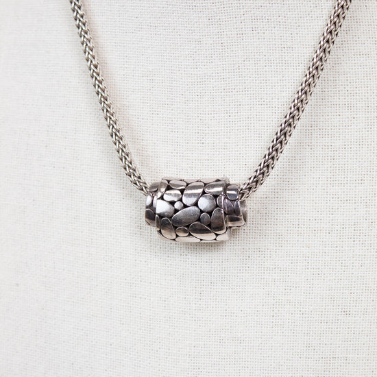 Silver necklace with a textured pendant on a light gray background