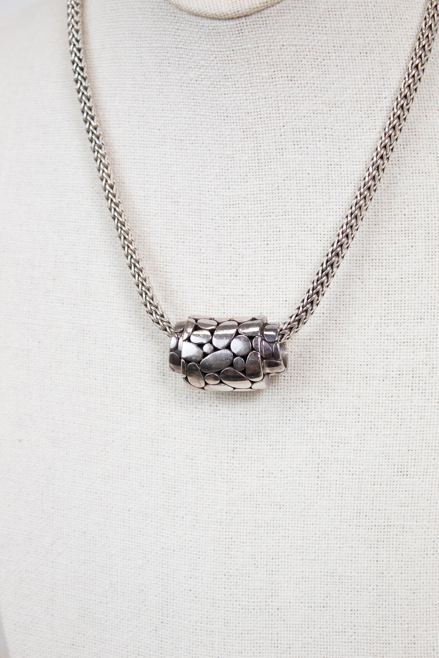 Silver necklace with a textured pendant on a light gray background