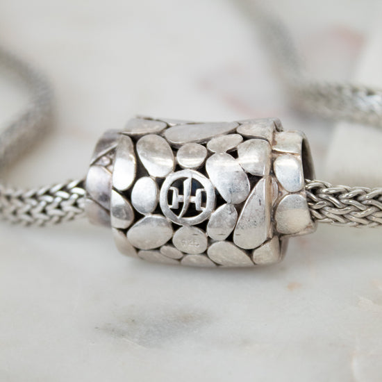 Close-up of a silver necklace with a detailed pendant on a marble surface