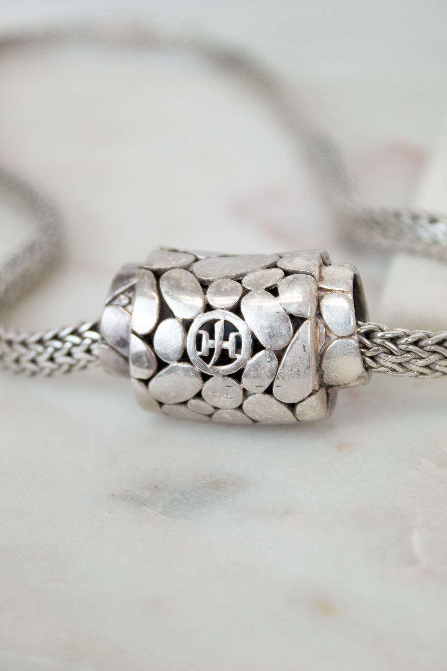 Close-up of a silver necklace with a detailed pendant on a marble surface