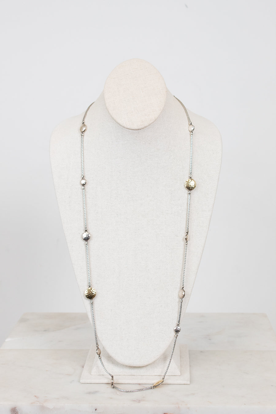 Long necklace with gold and silver beads on a mannequin head against a white background