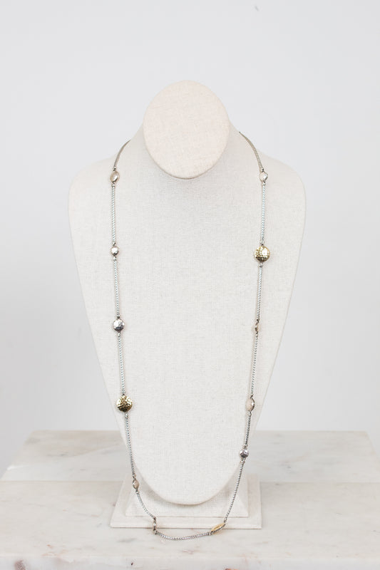 Long necklace with gold and silver beads on a mannequin head against a white background