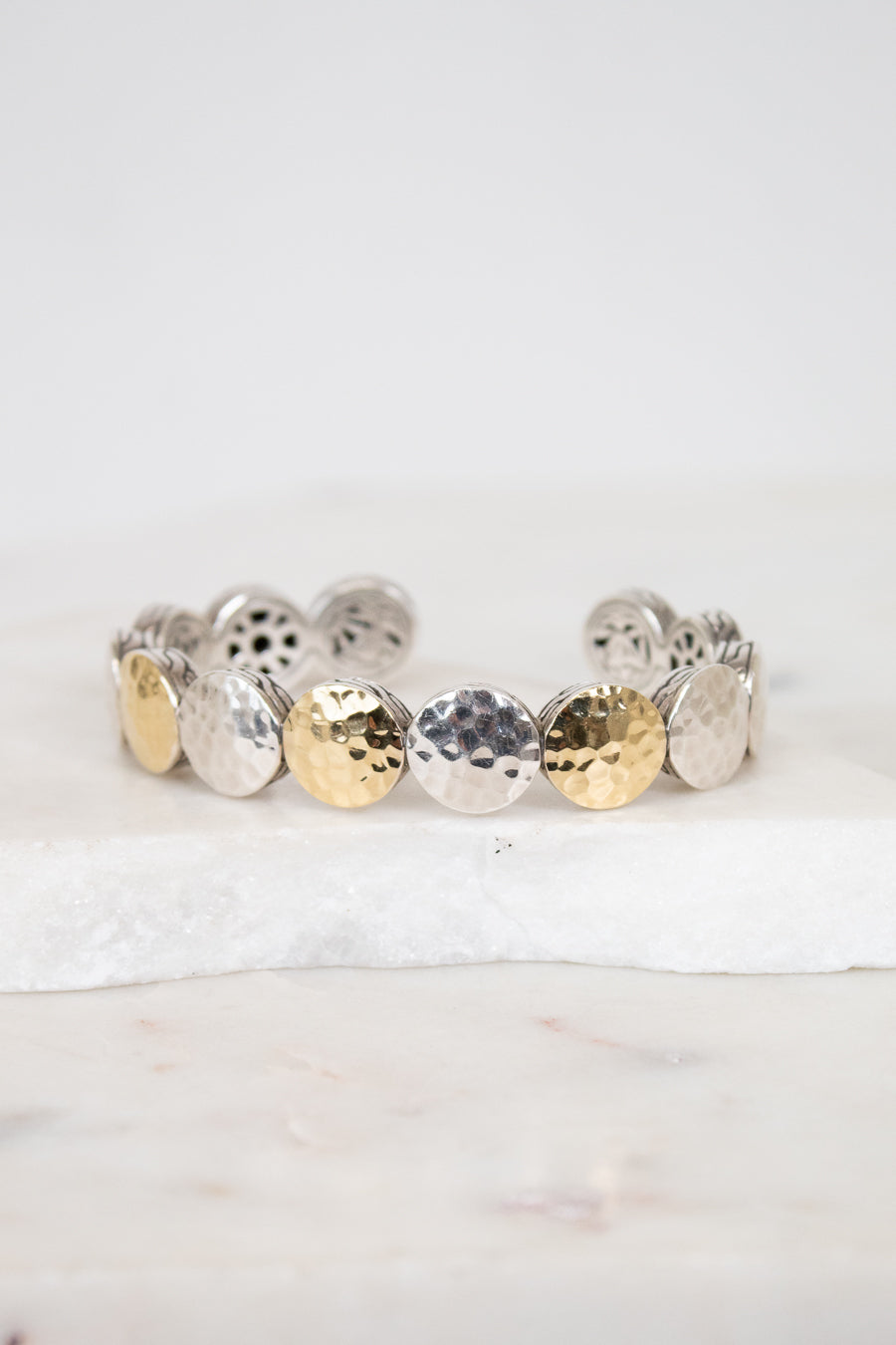 Bracelet with round, textured design in gold and silver on a white background