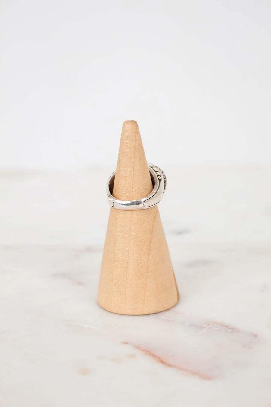 Silver ring on a wooden cone against a marble background
