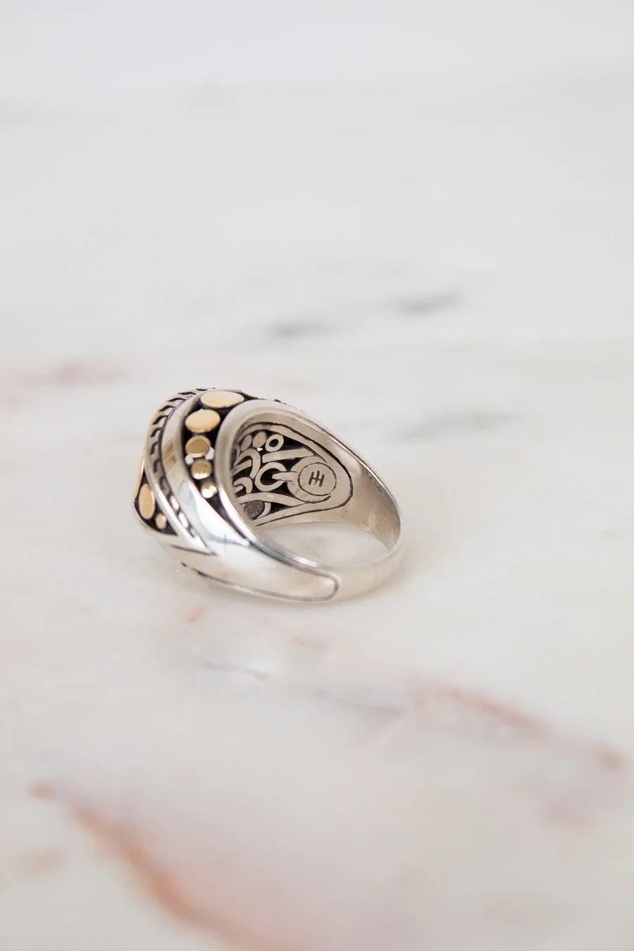 Silver ring with intricate design on a marble surface