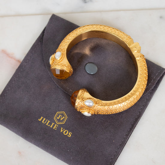 Gold bracelet with pearls on a dark pouch with 'Julie Vos' branding, on a marble surface.