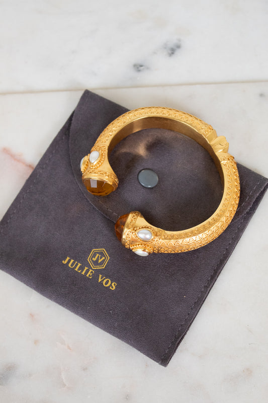 Gold bracelet with pearls on a dark pouch with 'Julie Vos' branding, on a marble surface.