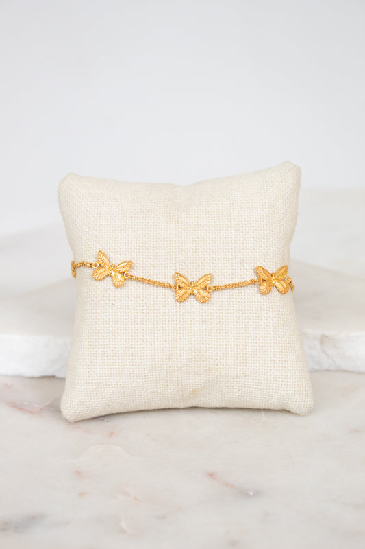 Gold bracelet with butterfly designs on a white pillow against a marble background