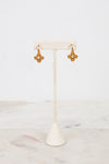 Gold earrings on a white earring stand with a white background