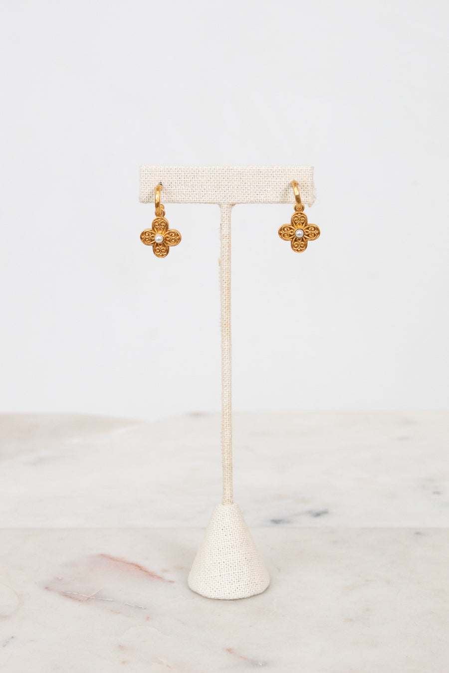 Gold earrings on a white earring stand with a white background