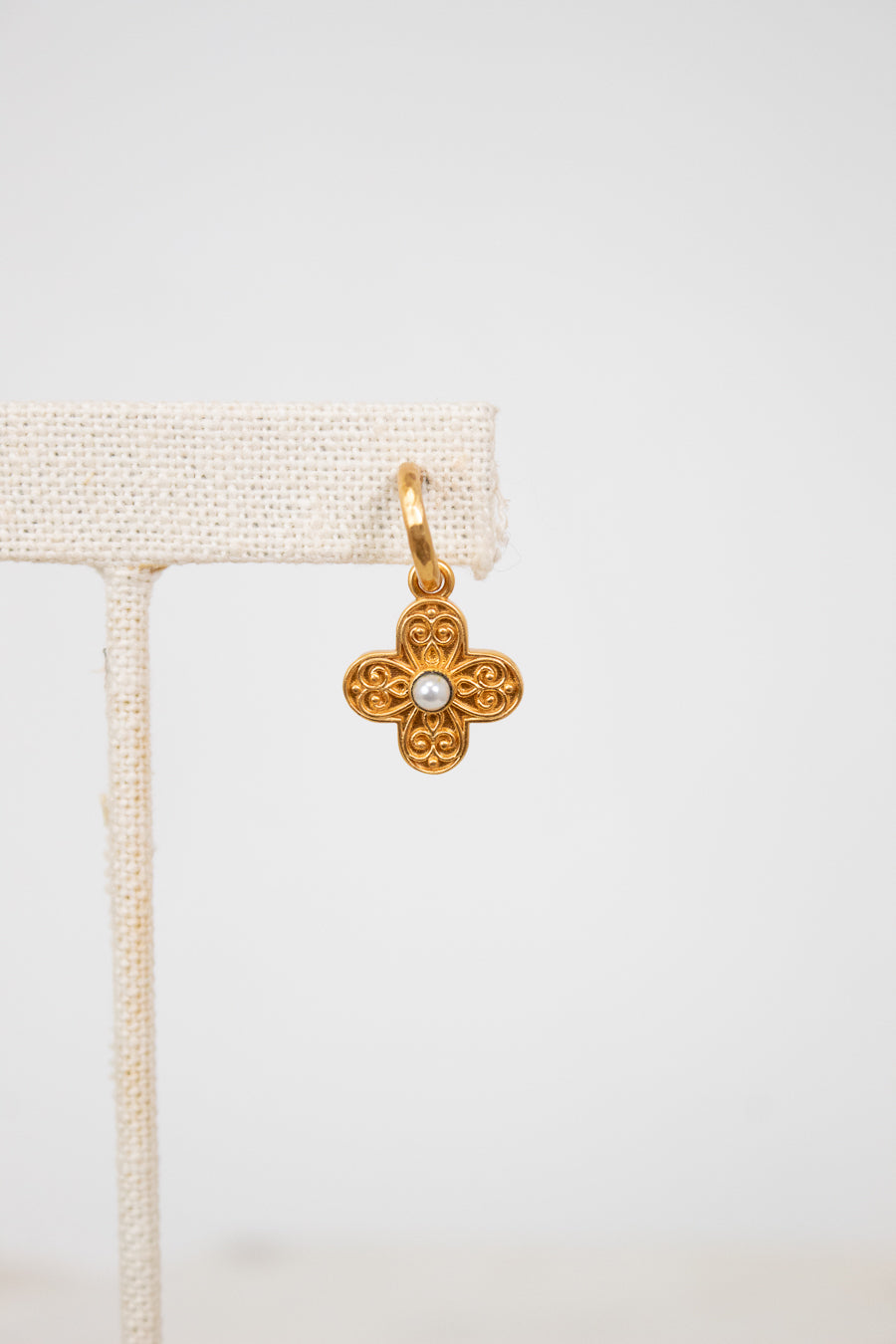 Gold flower-shaped earring with a pearl center on a white background