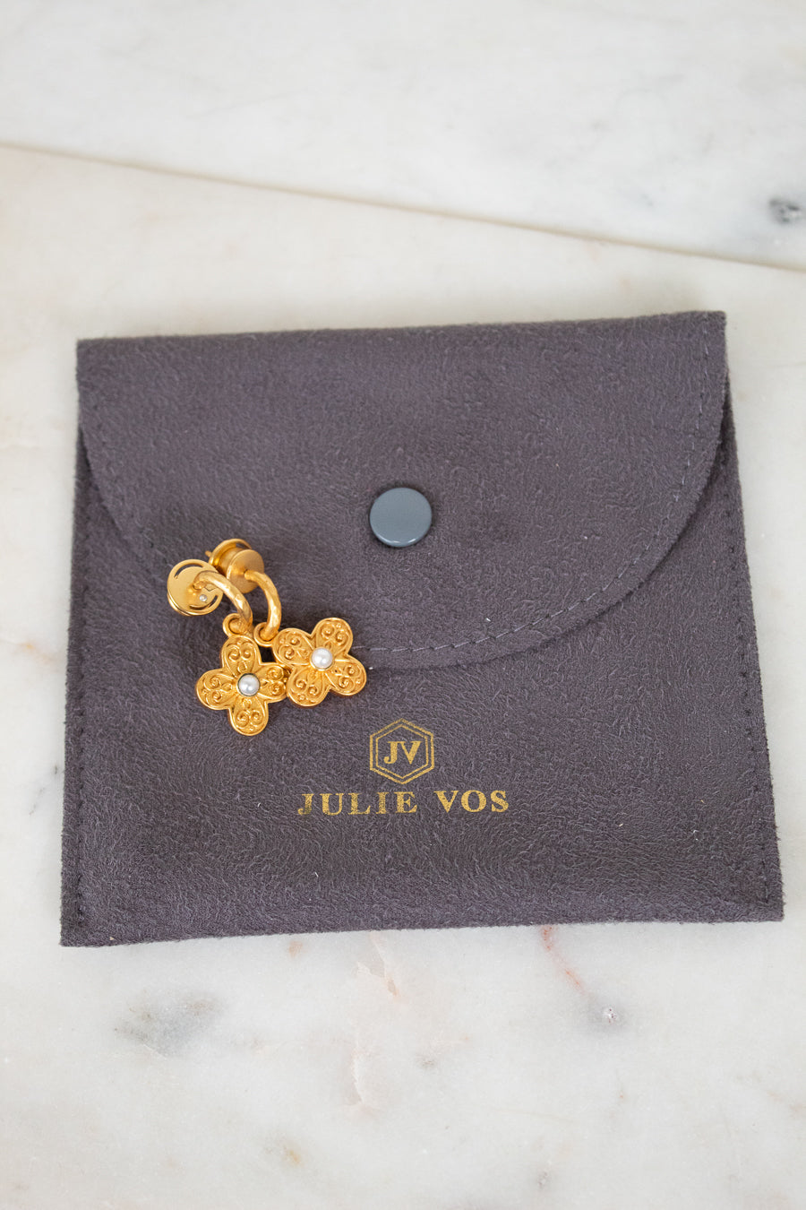 Gold floral earrings on a gray Julie Vos jewelry pouch.