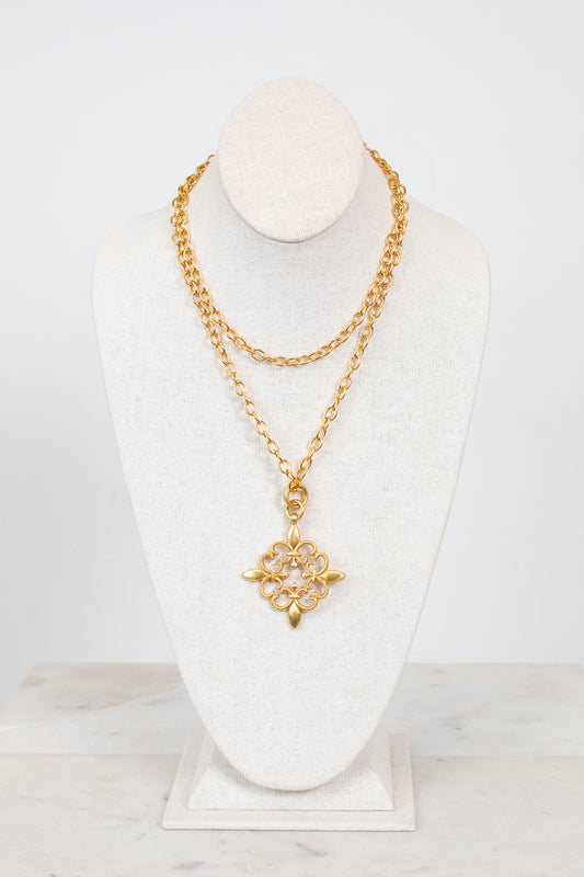 Gold necklace with a floral pendant on a white mannequin bust against a light gray background